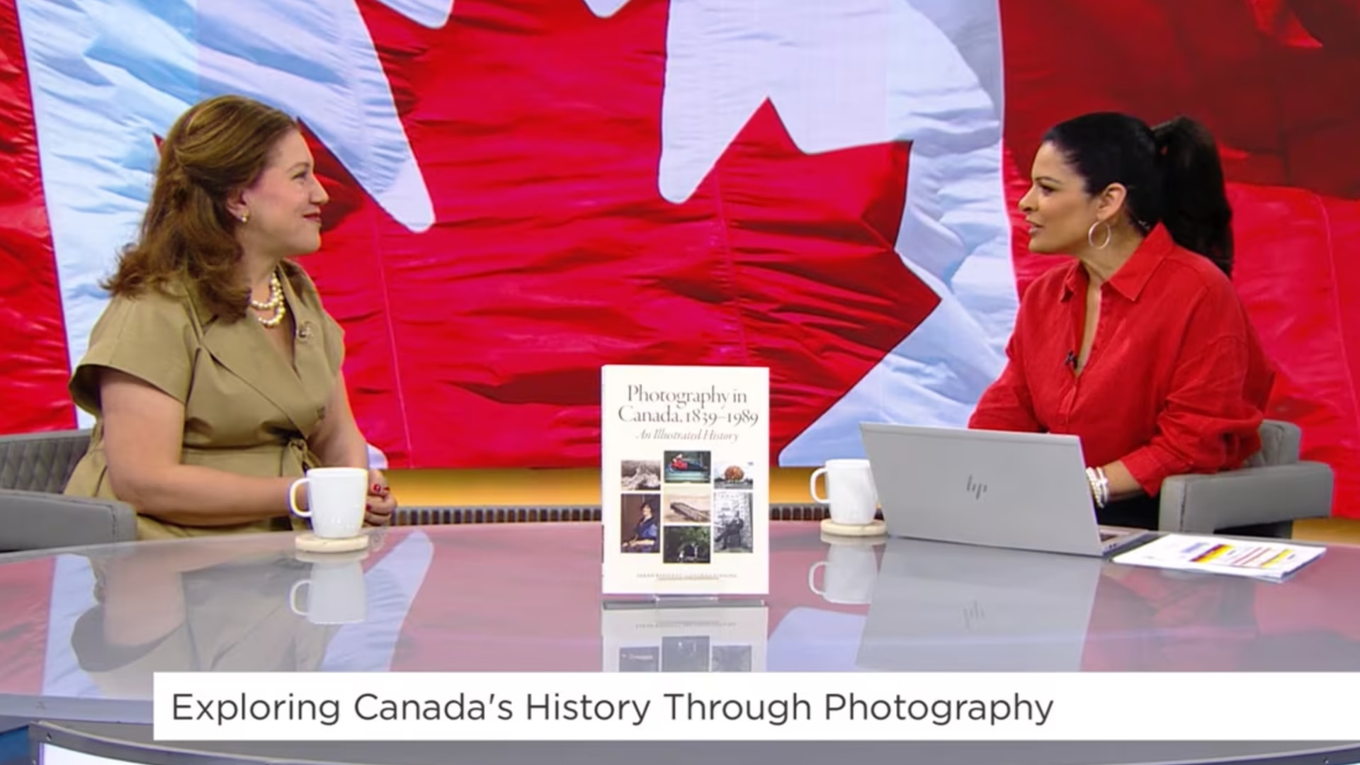 Sara Angel sitting beside Anne-Marie Mediwake with the book Photography in Canada in between them on a desk